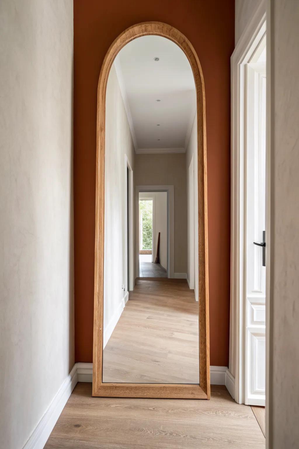 An arched mirror turns the end of a narrow hallway into a calm, light‑opening “doorway”.